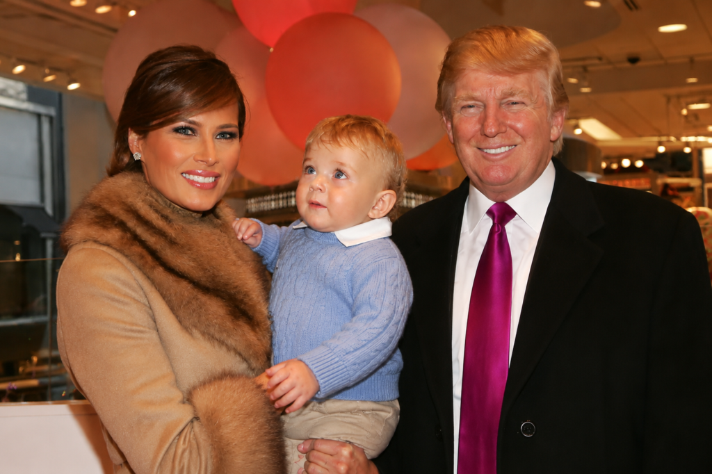 Donald Trump and Melania Trump smiling while holding their infant son Barron Trump at a public event.