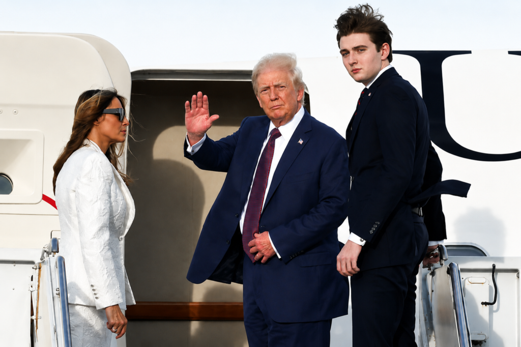 Donald Trump waving alongside Melania Trump and teenage son Barron Trump while standing at the stairs of an airplane.